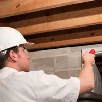 Termite inspection technician checking a basement wall and framing for termite activity in Manchester, NH